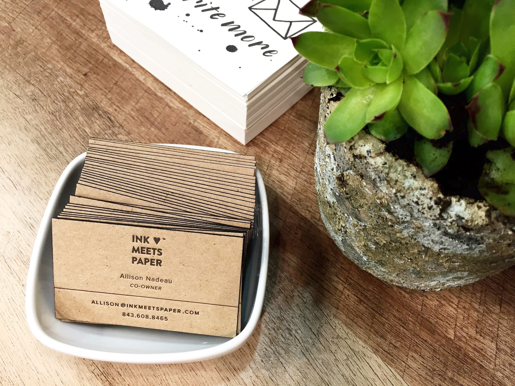 A scene showing INK MEETS PAPER business cards sitting in a tray along with a small succulent plant.
