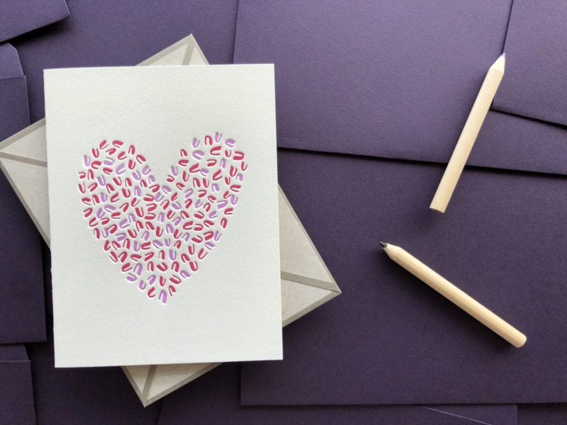 Two-color greeting card on bed of purple envelopes and two wooden pencils