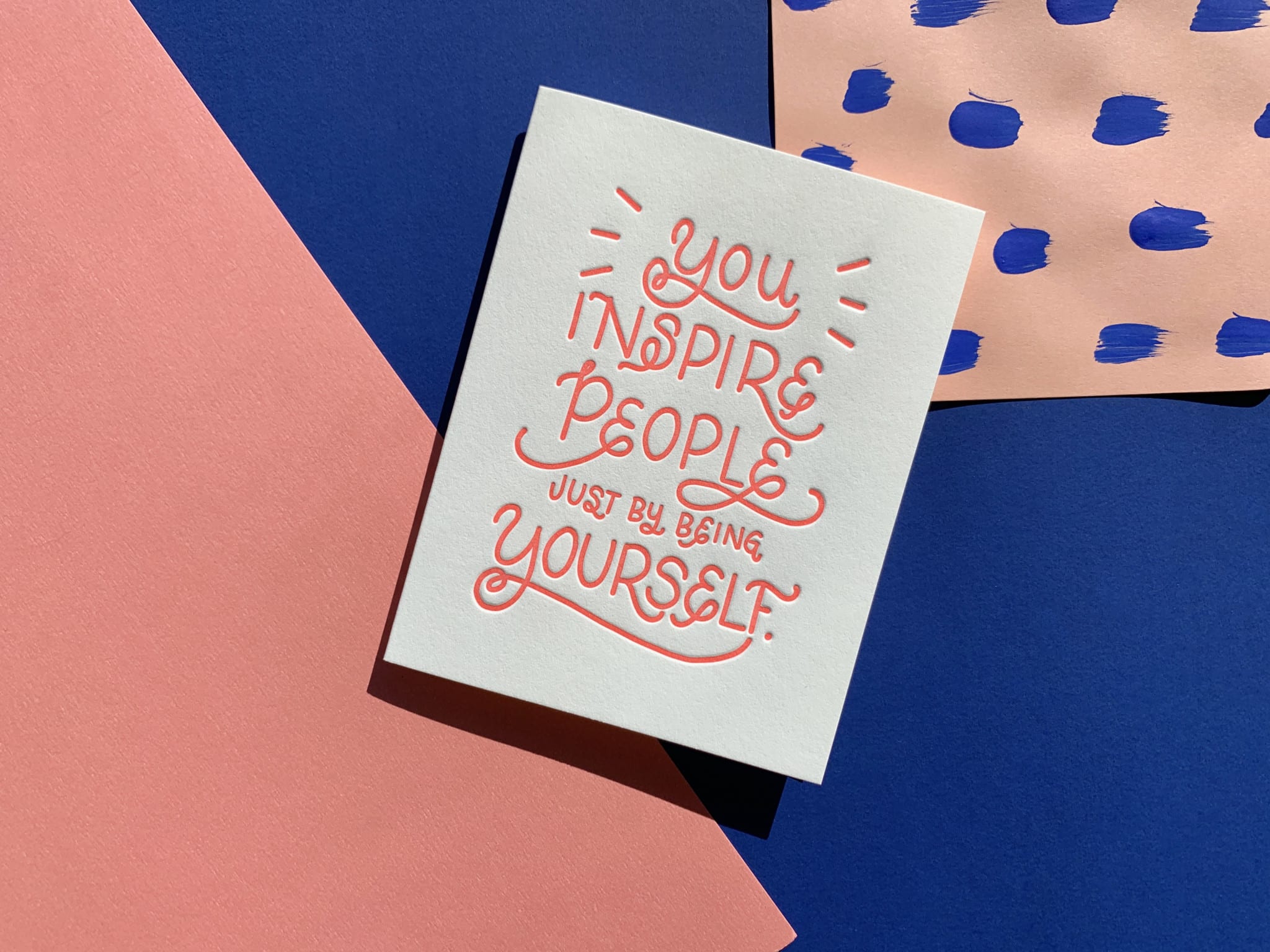 Bright colored handlettering highlights a letterpress printed card on a multi-layered paper background.