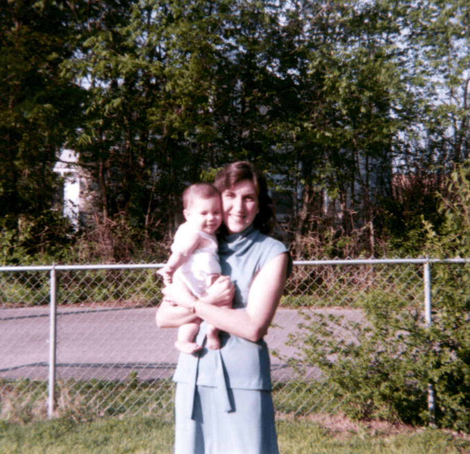 old photograph of Allison's Mother holding her outside with a chain-link fence in the background