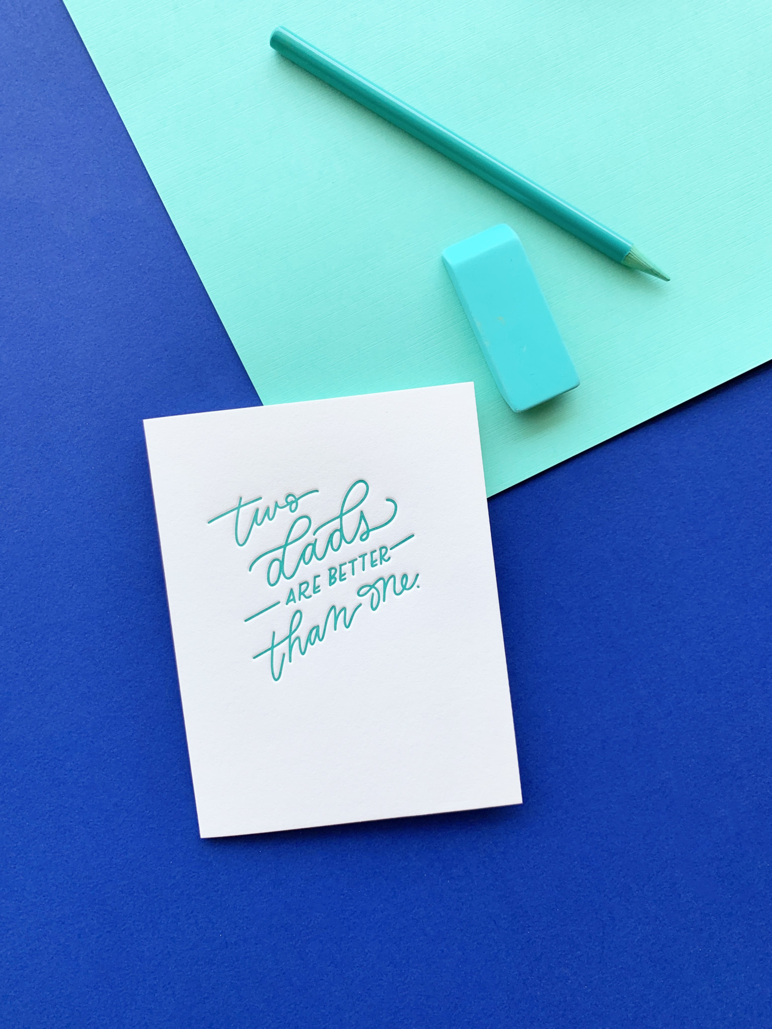 Two Dads Letterpress greeting card on layered blue paper background with eraser and pencil accents.