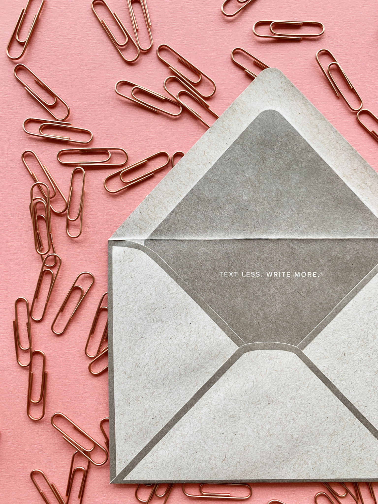 INK MEETS PAPER® Signature Envelope on a pink paper background surrounded by gold paper clips