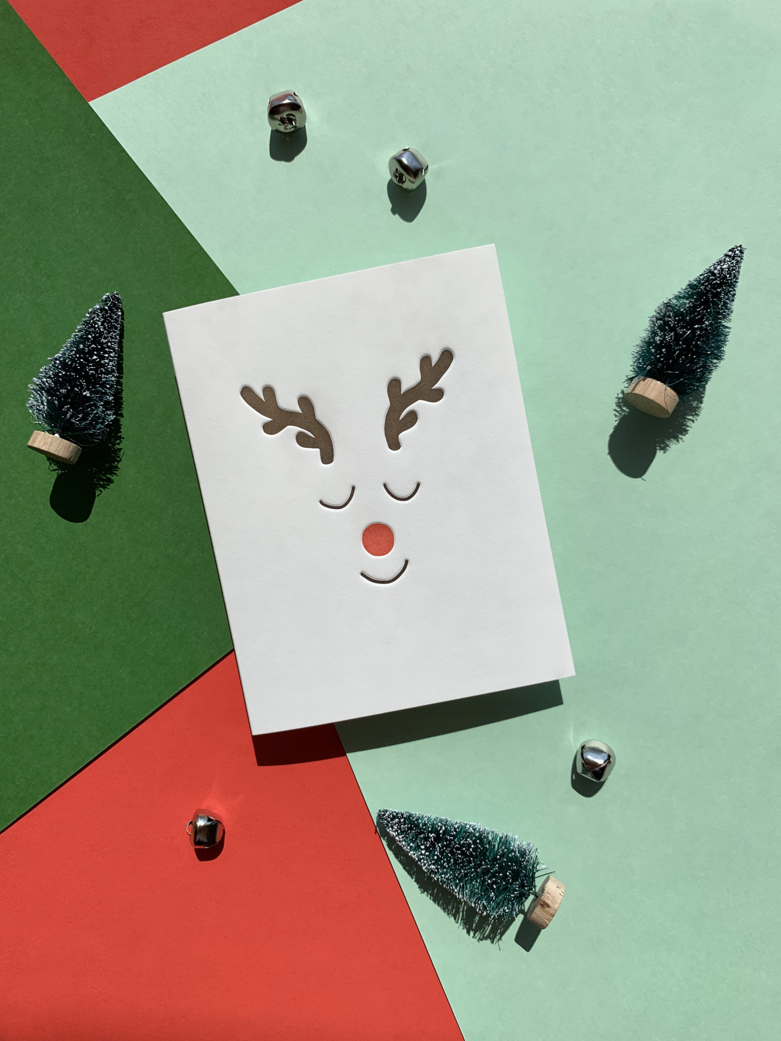 Antlers, a red nose, and eyelid lines show a minimalist Rudolph on this white cotton card.