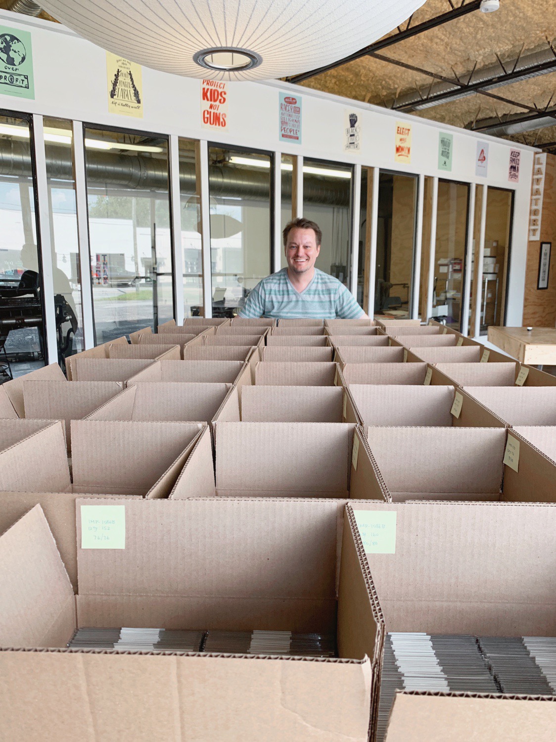 Team member stands at the back of a table filled with boxes that contain greeting cards assembled for a large order