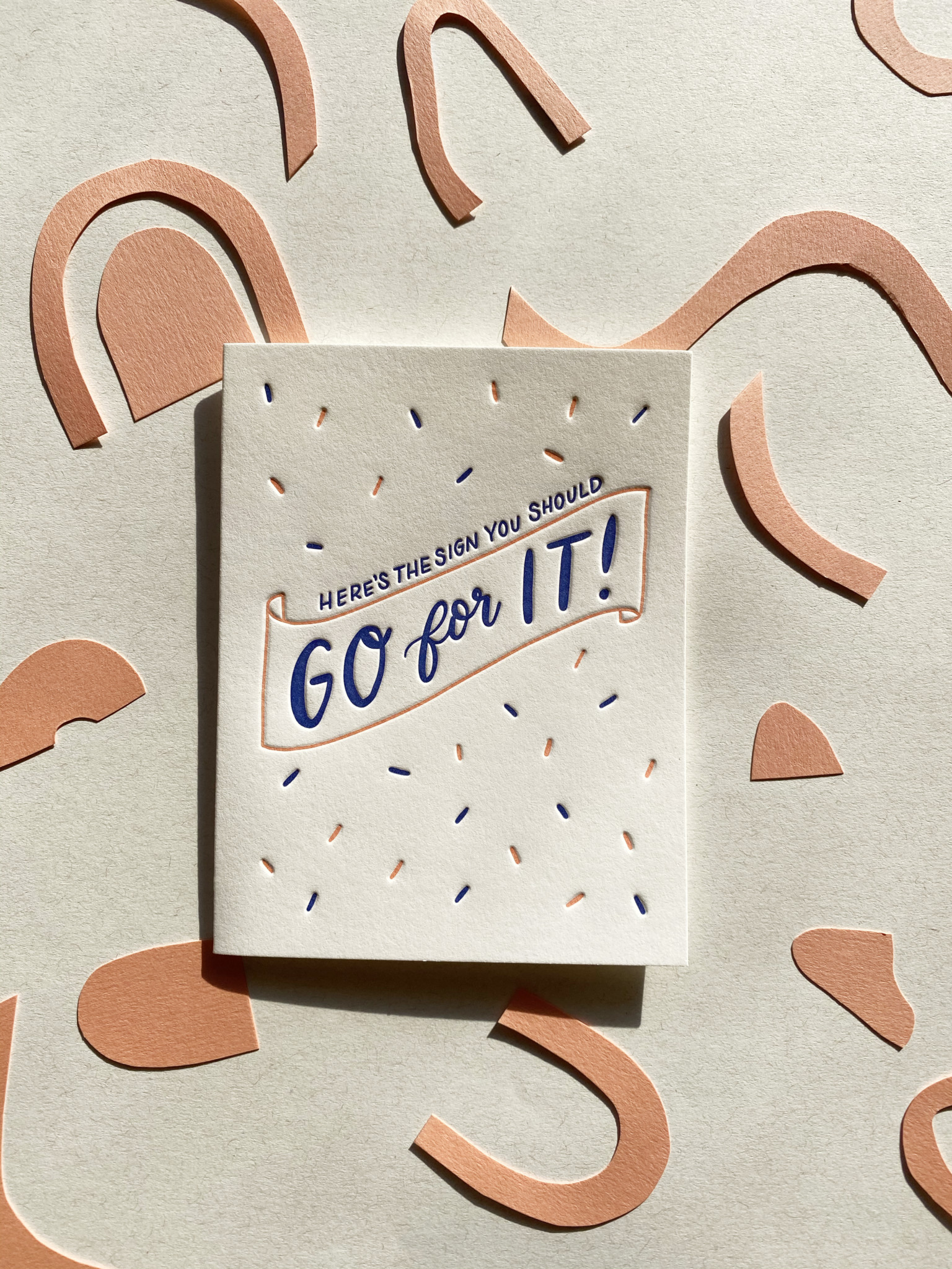 Front of letterpress-printed greeting card has coral and bright blue confetti and a coral banner that states "Here's the sign you should Go for It!"